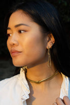 Woman wearing long abstract loop earrings and gold figure eight knot herringbone choker necklace 