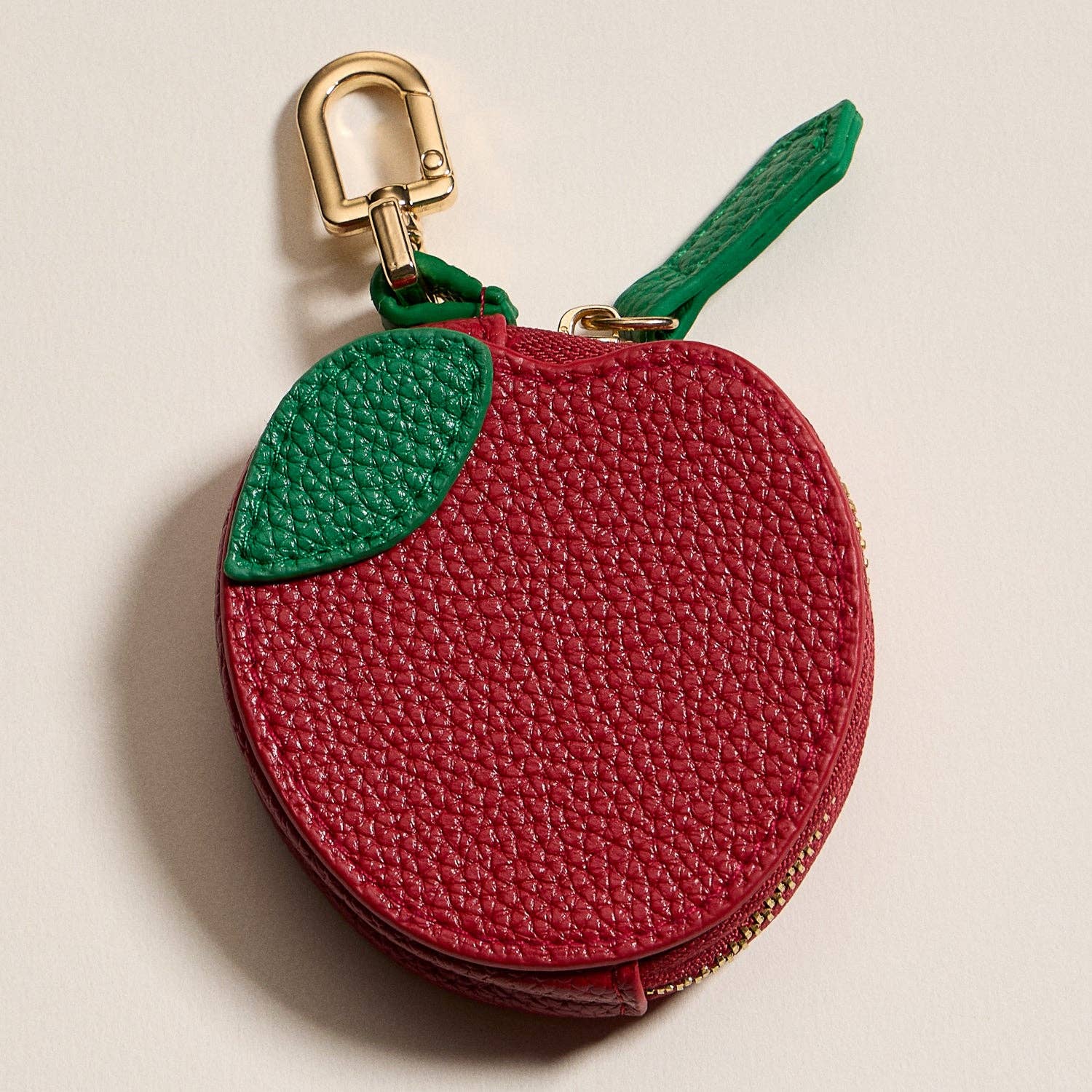 Red apple-shaped keychain purse with a gold clasp on a beige background