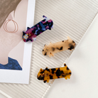 Three cat barrettes in brown, tan and blue laying on textured surface