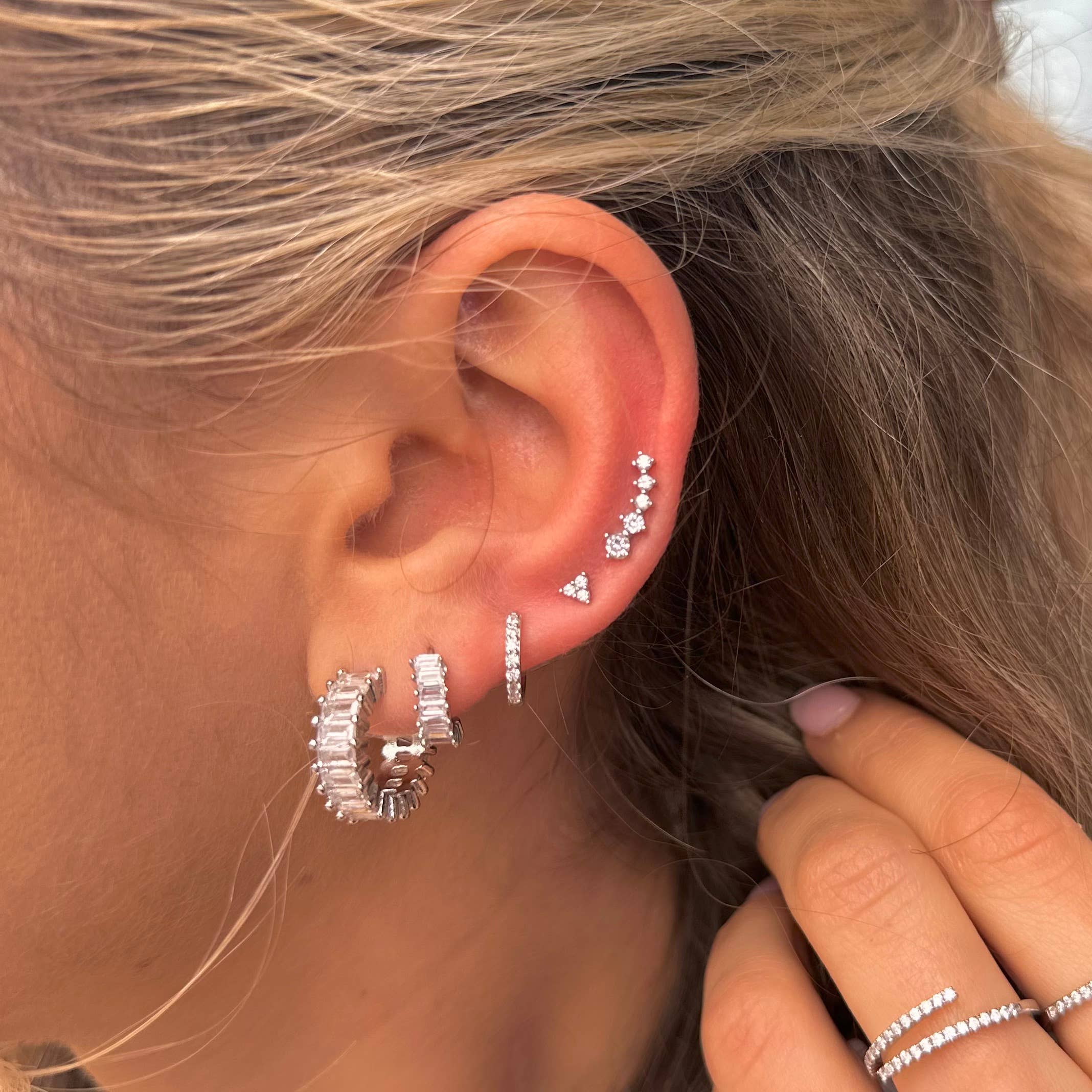 Woman wearing earring stack with silver diamond huggie earrings 
