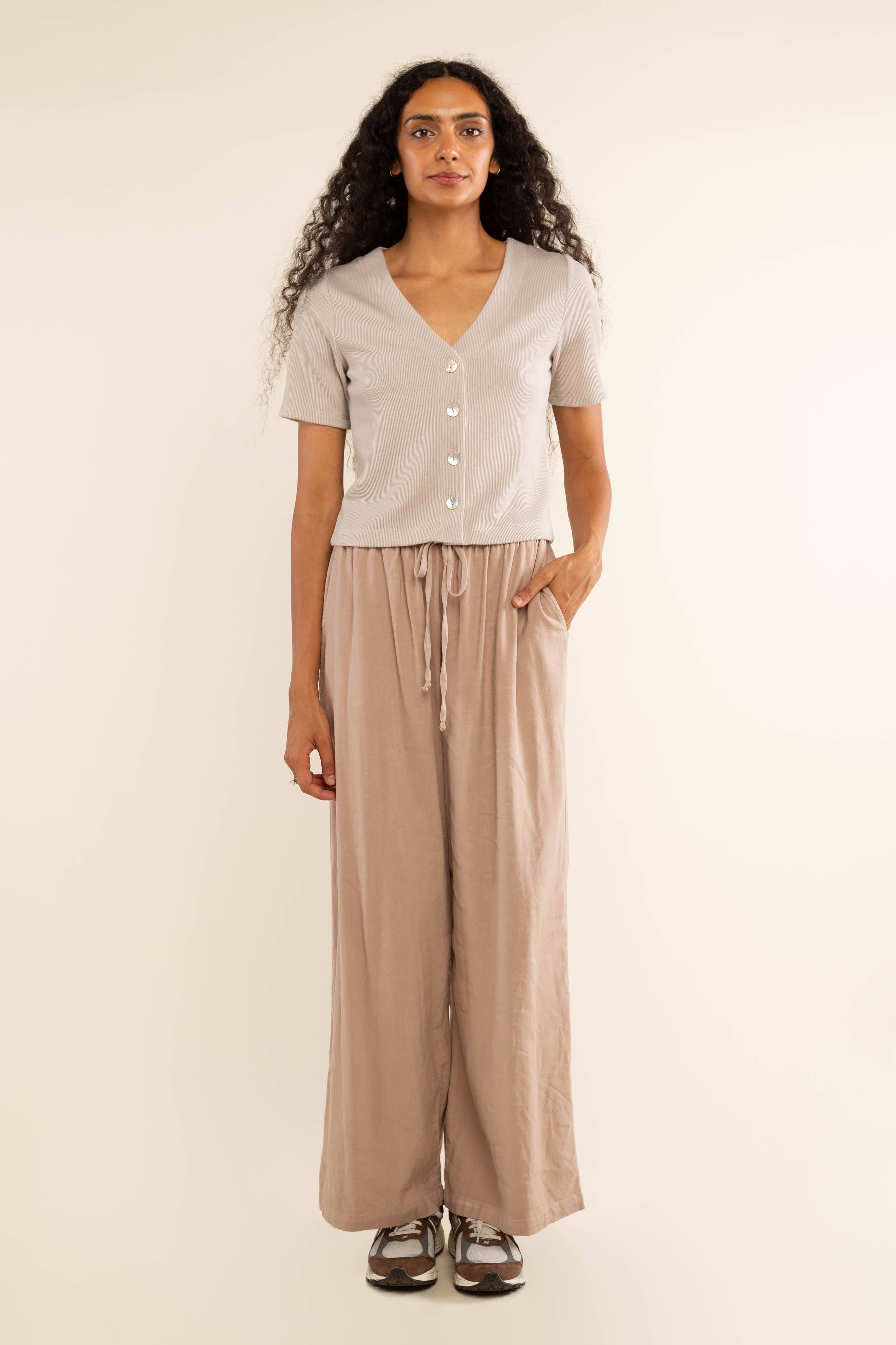 Woman wearing oat colored, ribbed, button down, short sleeve blouse top and beige pants 