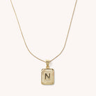 Letter N tarnish free gold initial charm necklace behind a blank background. 