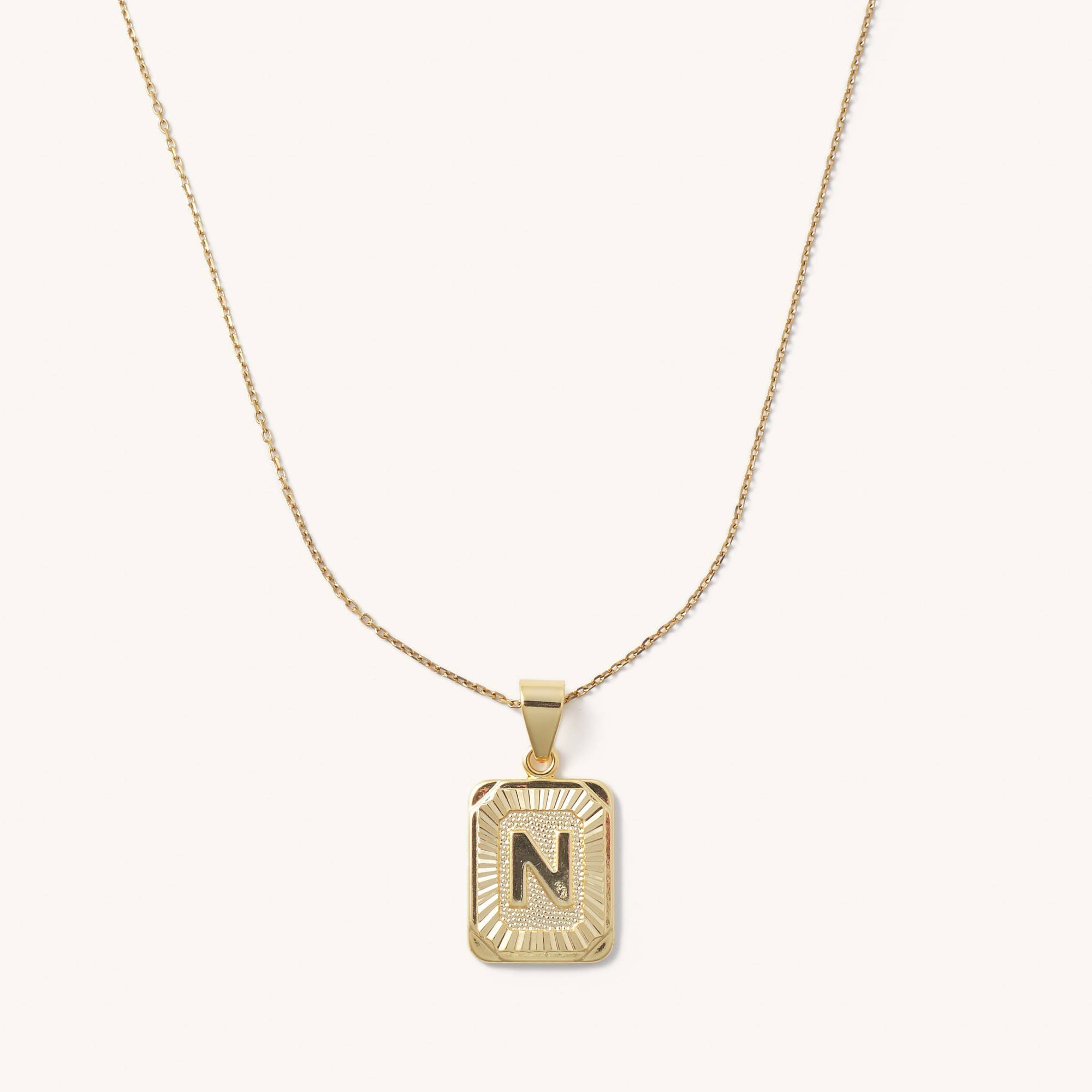 Letter N tarnish free gold initial charm necklace behind a blank background. 