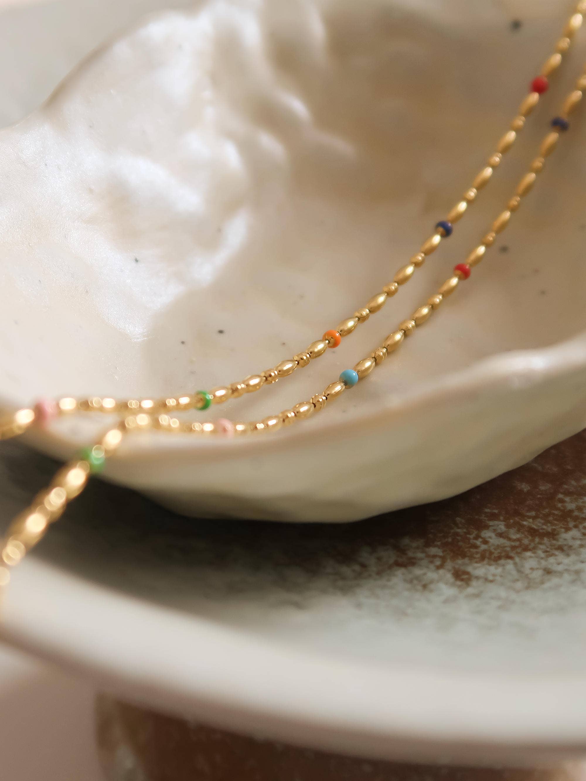 Two gold necklaces with colorful beads on a white shell