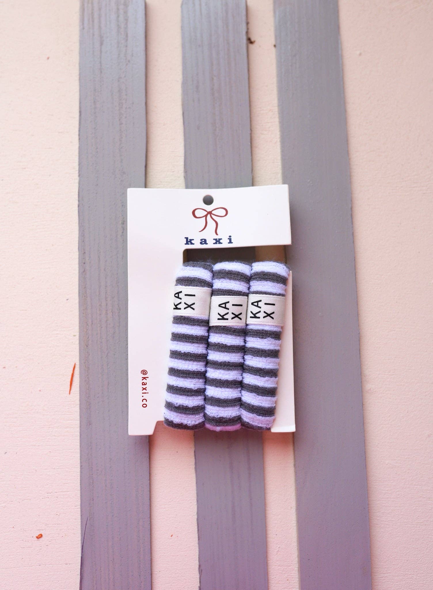 Striped socks on a pink and gray striped background with 'kaxi' branding.
