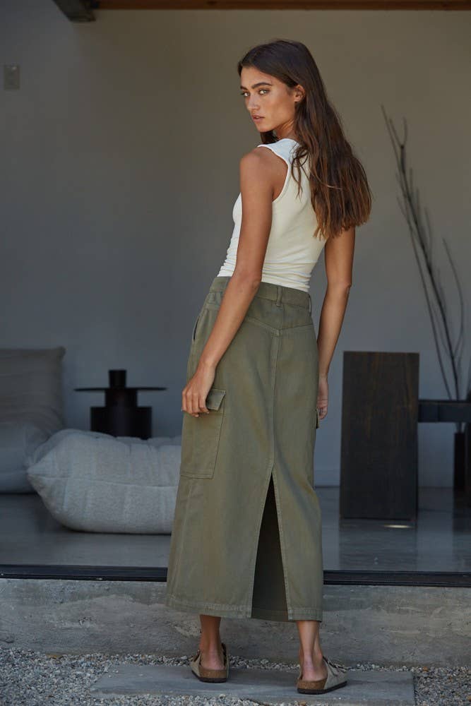 Woman wearing a white tank top and green pants standing in a modern indoor setting.