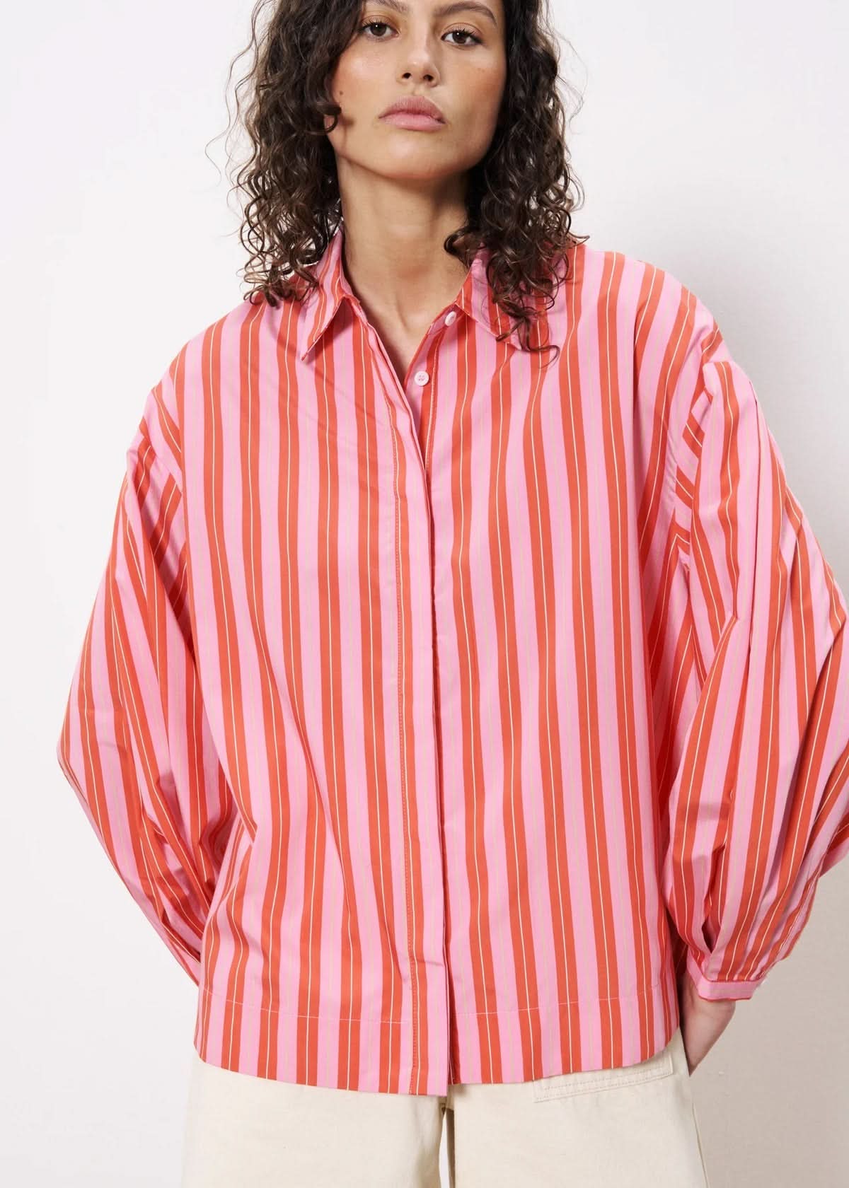 Woman wearing long sleeve button down satin blouse with red and pink stripes 