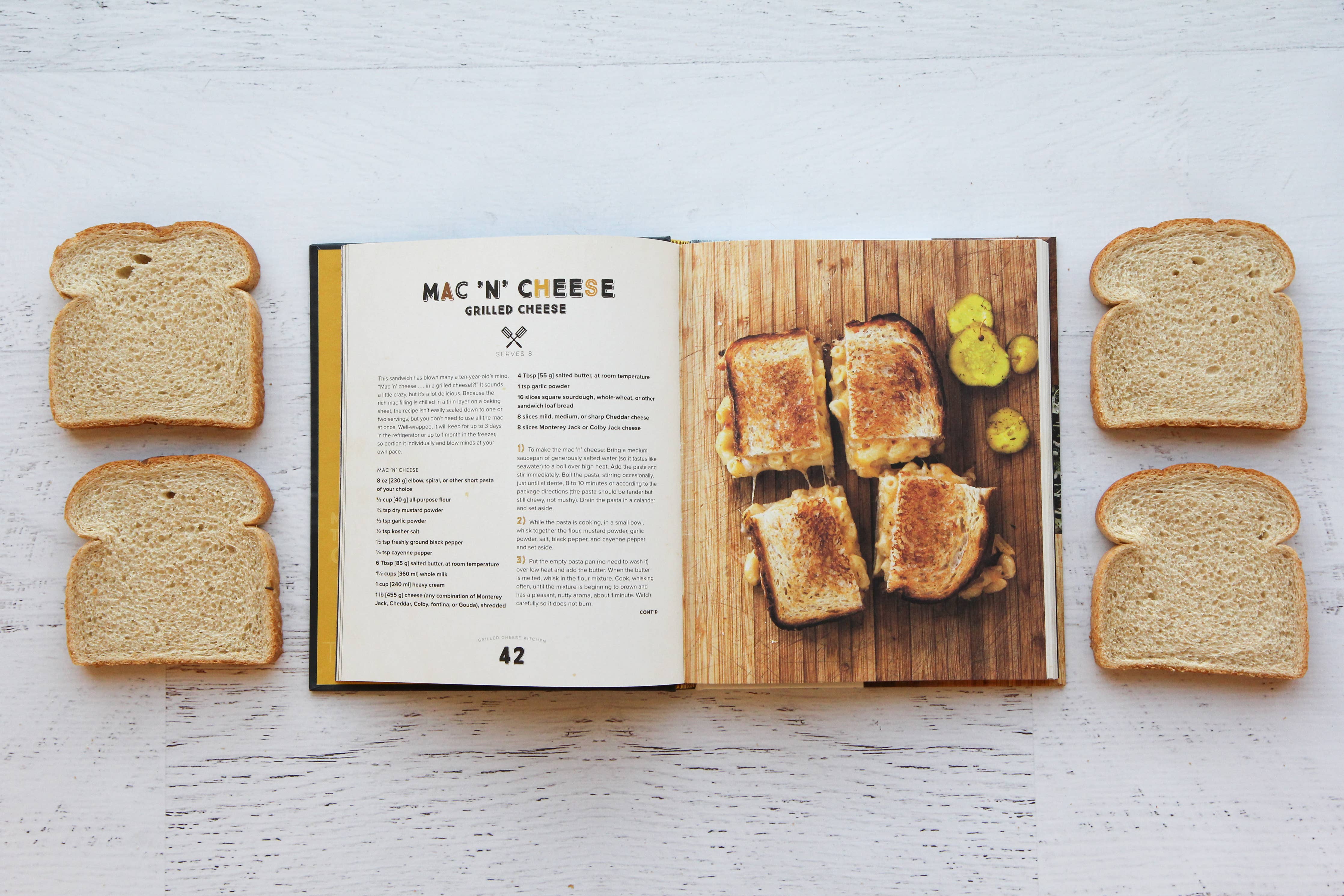 Open cookbook showing a grilled cheese recipe with slices of bread on a white surface