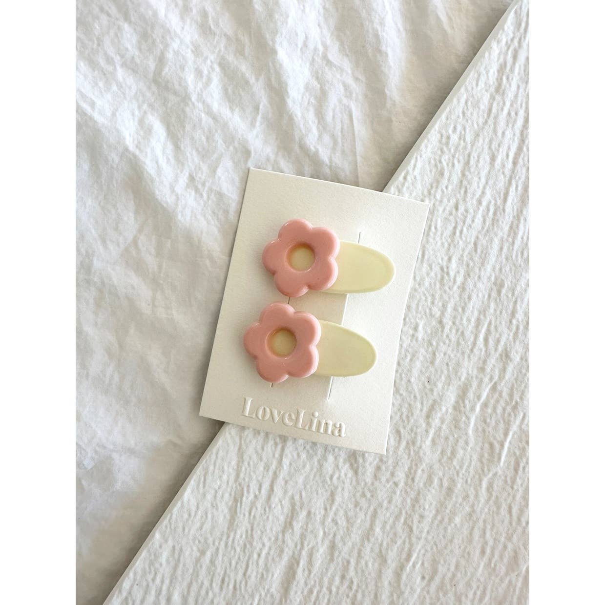 Pair of mini pink and white flower clips clipped to display card laying on white cloth