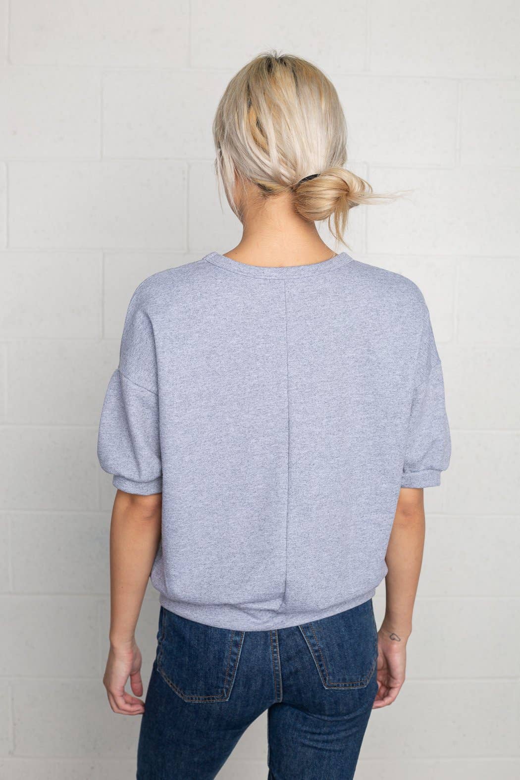 Woman facing away from the camera wearing natural grey, short sleeve, puff sleeve, blouse t-shirt top, with vertical indent line down the back 