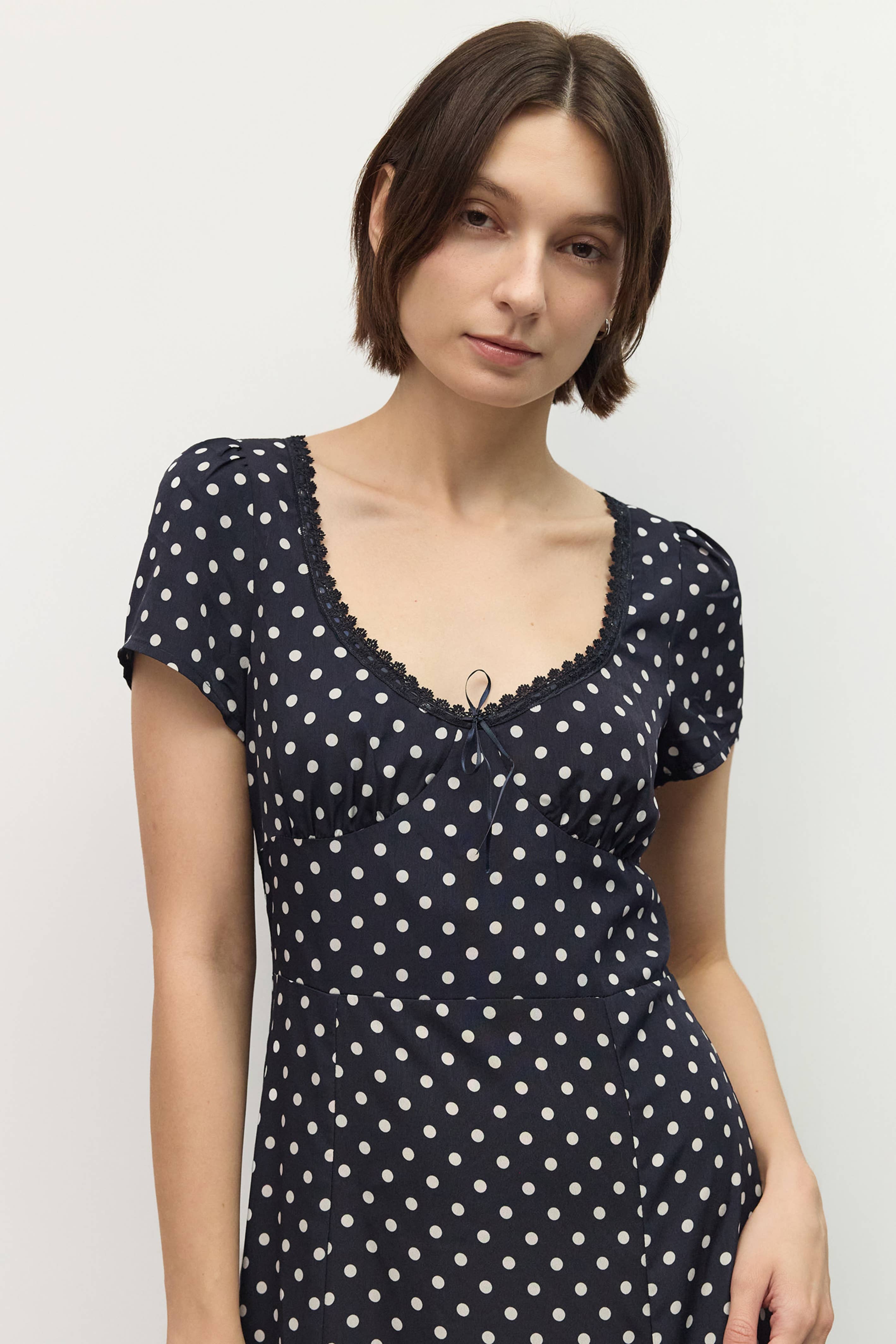 Woman wearing a navy blue dress with white polka dots against a plain background