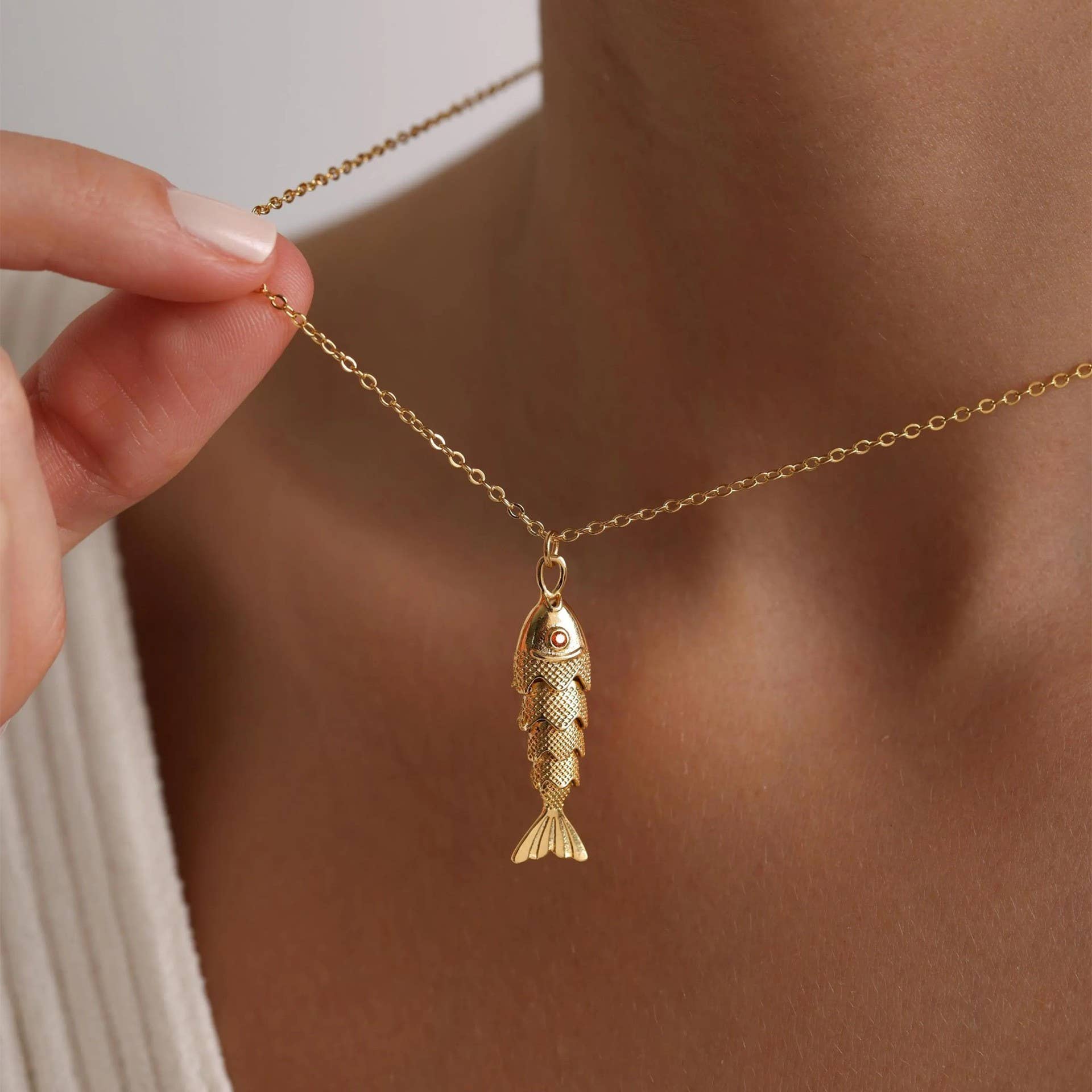 Gold fish pendant necklace being held by a hand against a neutral background