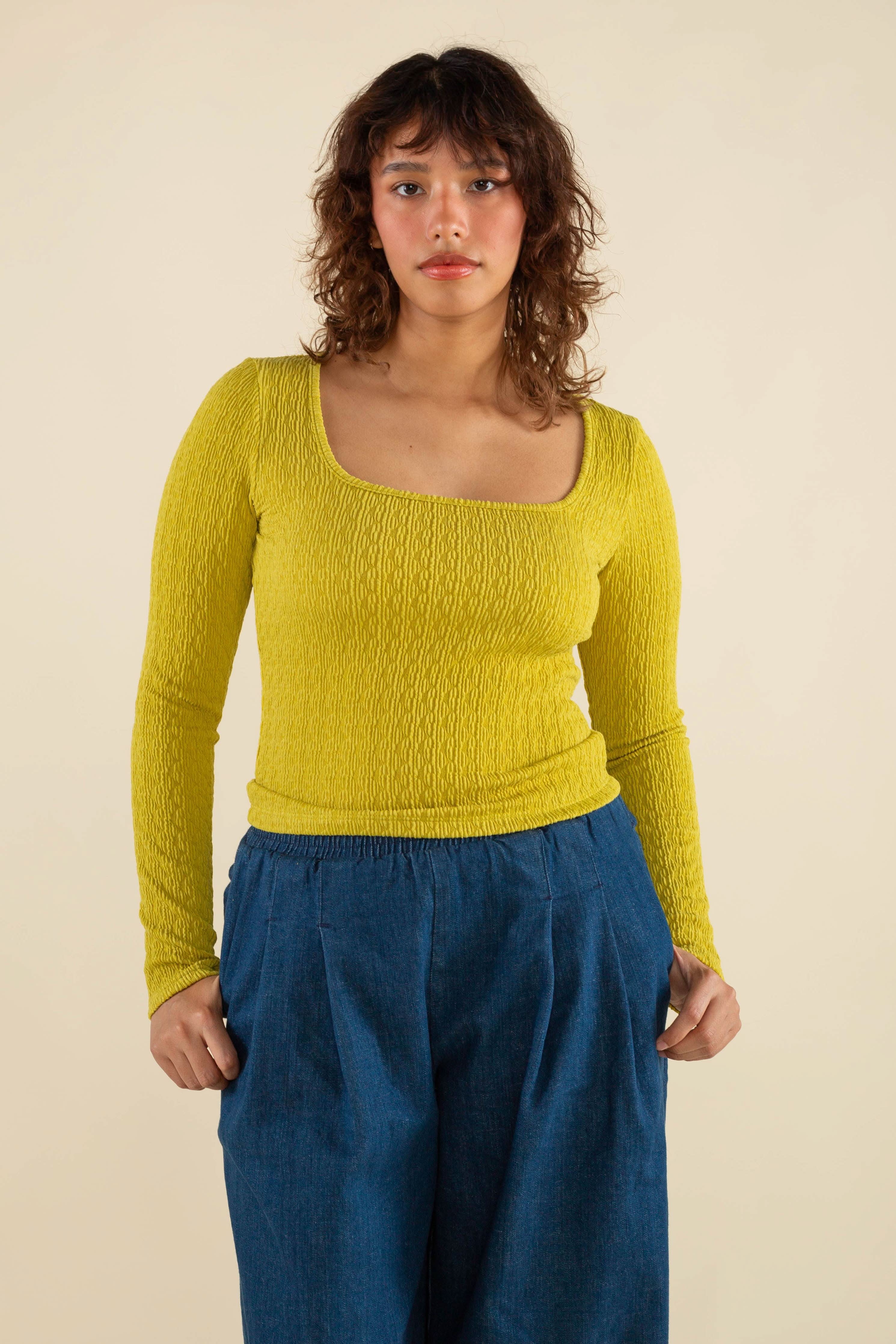 Woman wearing chartreuse, square neck line, textured, long sleeve top and jeans 