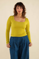 Woman wearing chartreuse, square neck line, textured, long sleeve top and jeans 