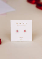 tiny pink heart-shaped opals set in a gold three-prong stud displayed on earring card with beige background