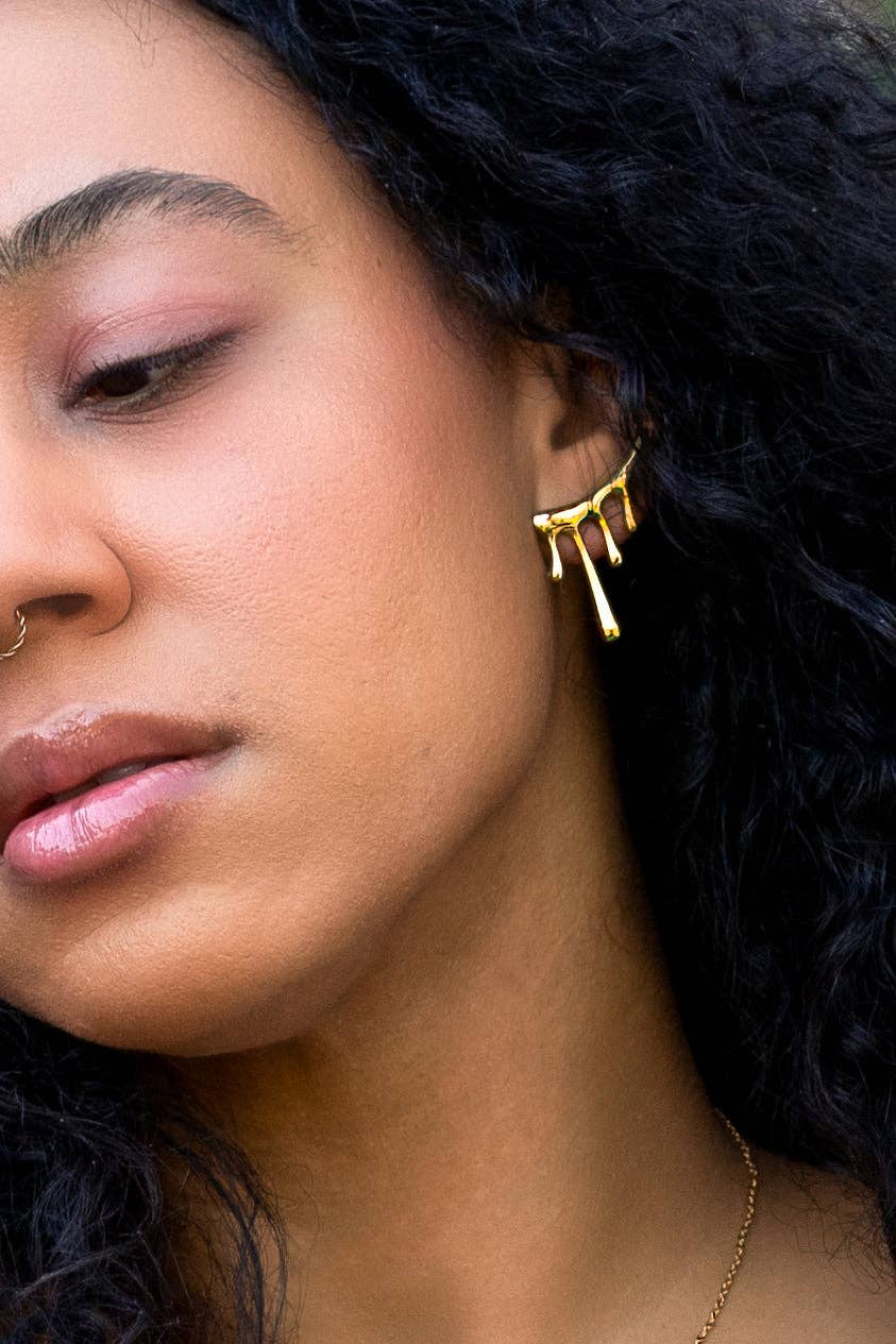 Woman wearing gold abstract earring with four solid dangle lava drips 