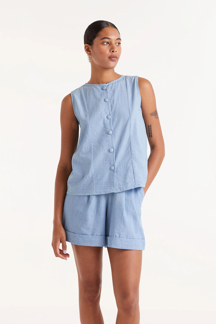 Woman wearing  blue denim like sleeveless  button down top and matching shorts