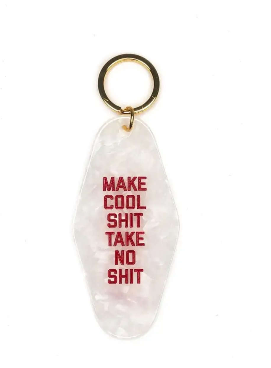 White marbled motel keychain that has red letters that say Make Cool Shit Take No Shit