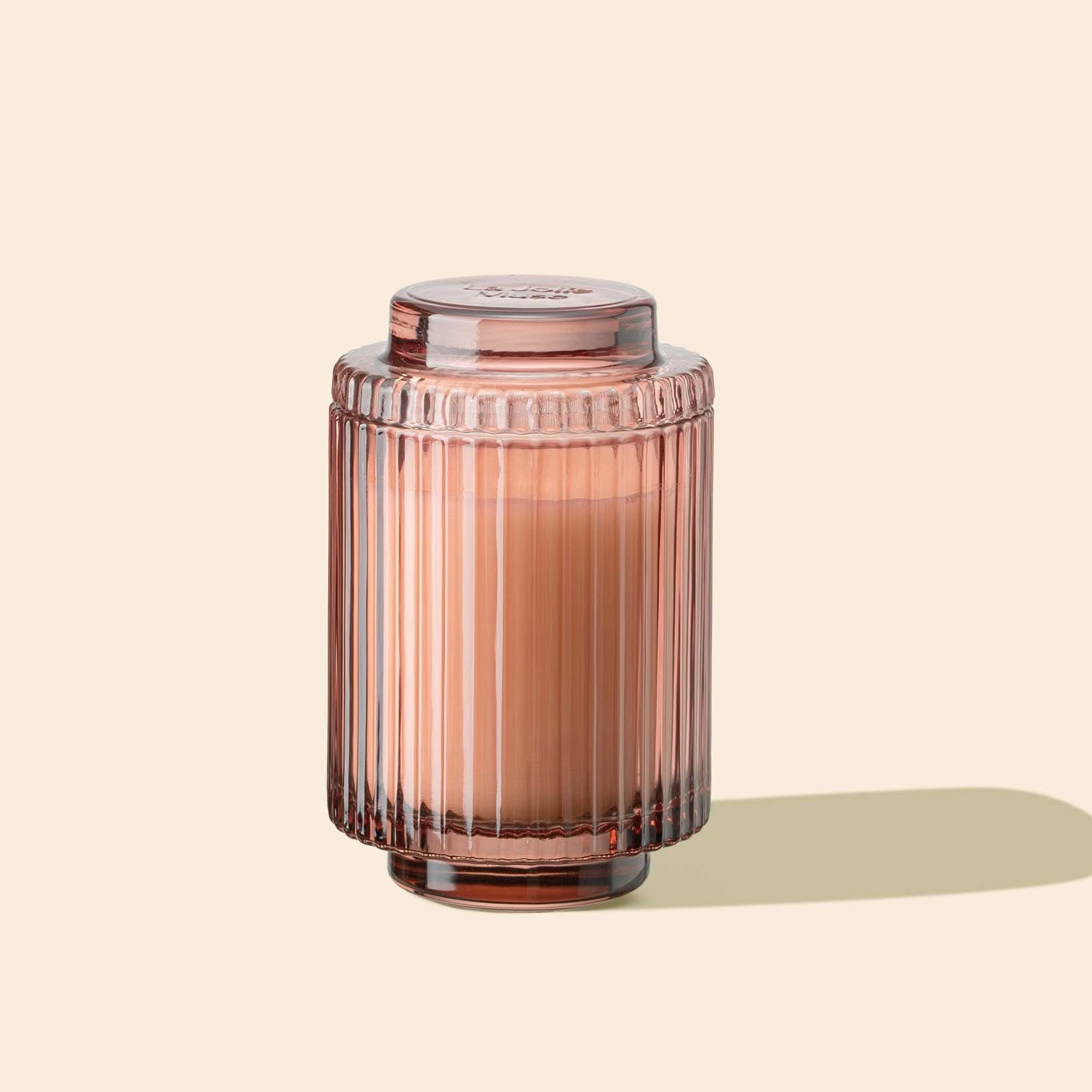 Pink glass candle jar with ribbed texture on a beige background