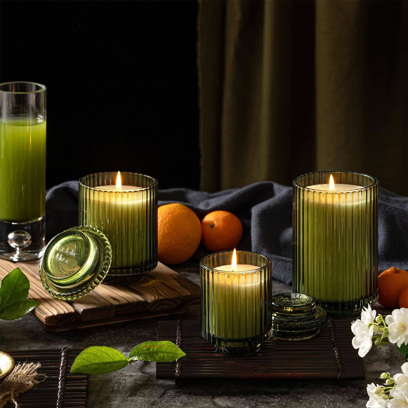 Green candles in glass holders with a glass of green juice and oranges on a dark background