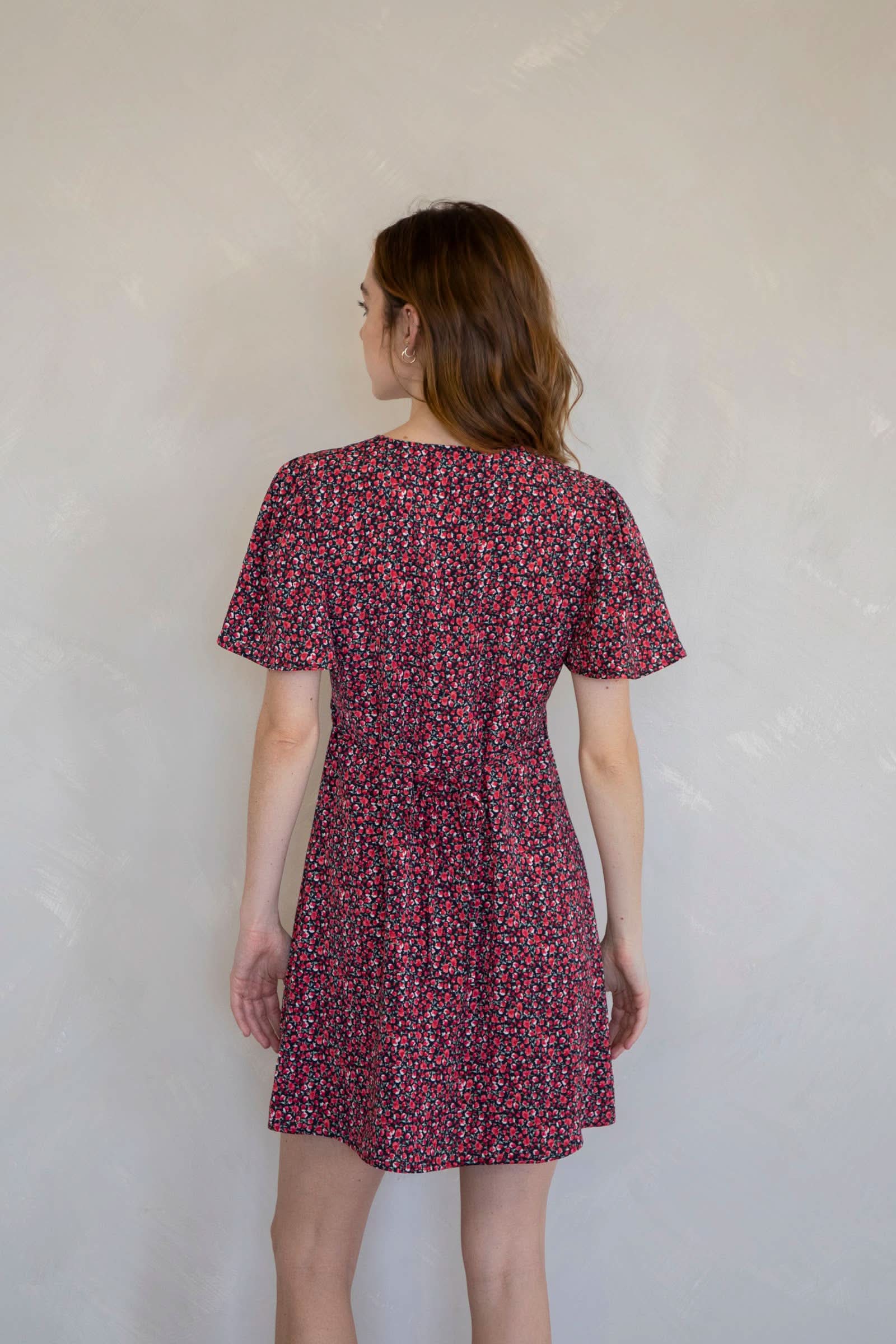 Woman wearing a red floral dress against a white wall