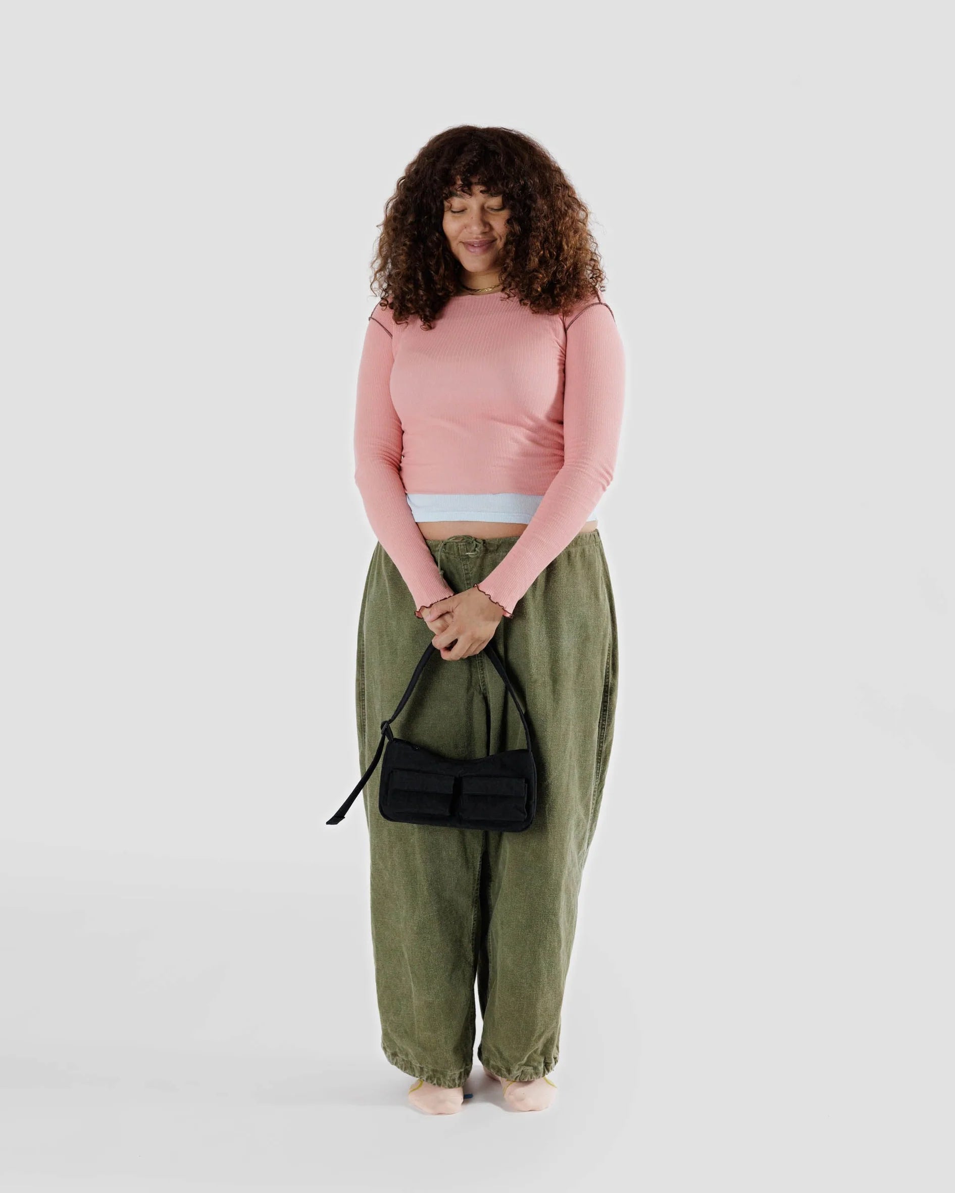 Woman wearing a pink top and green pants holding a black Cargo Shoulde Bag