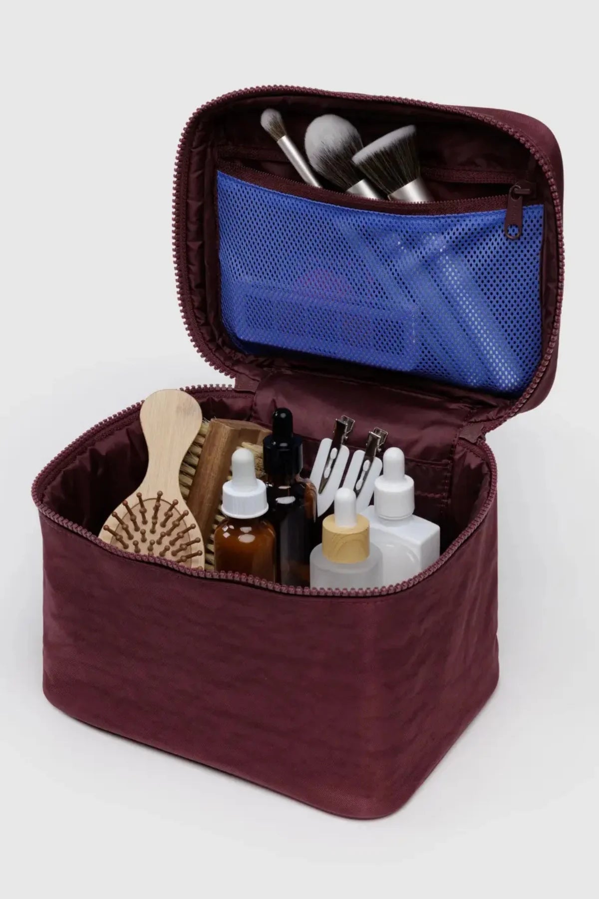 Open makeup bag with brushes, bottles, and a comb on a white background