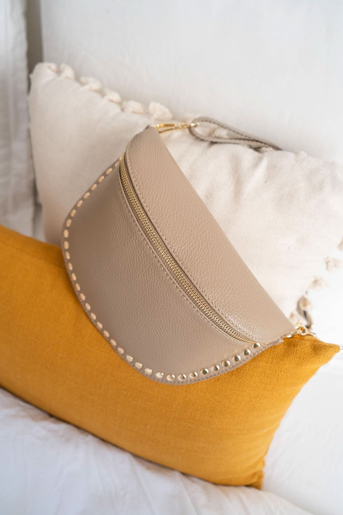 Beige pouch with decorative studs on a yellow pillow against a white background