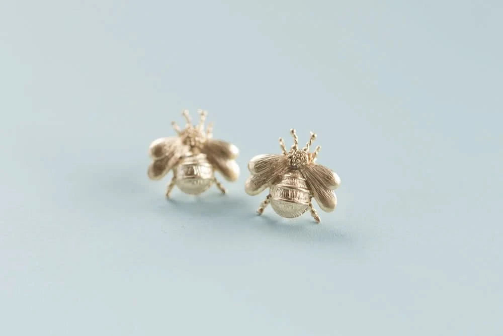 Gold bee-shaped earrings on a light blue background