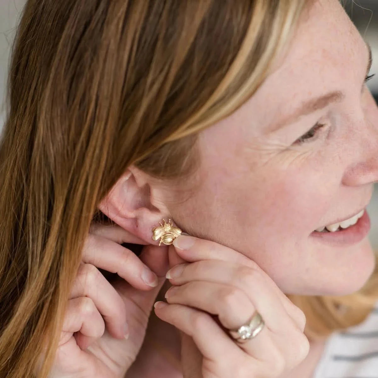 Woman wearing a gold earring and adjusting it with her fingers.