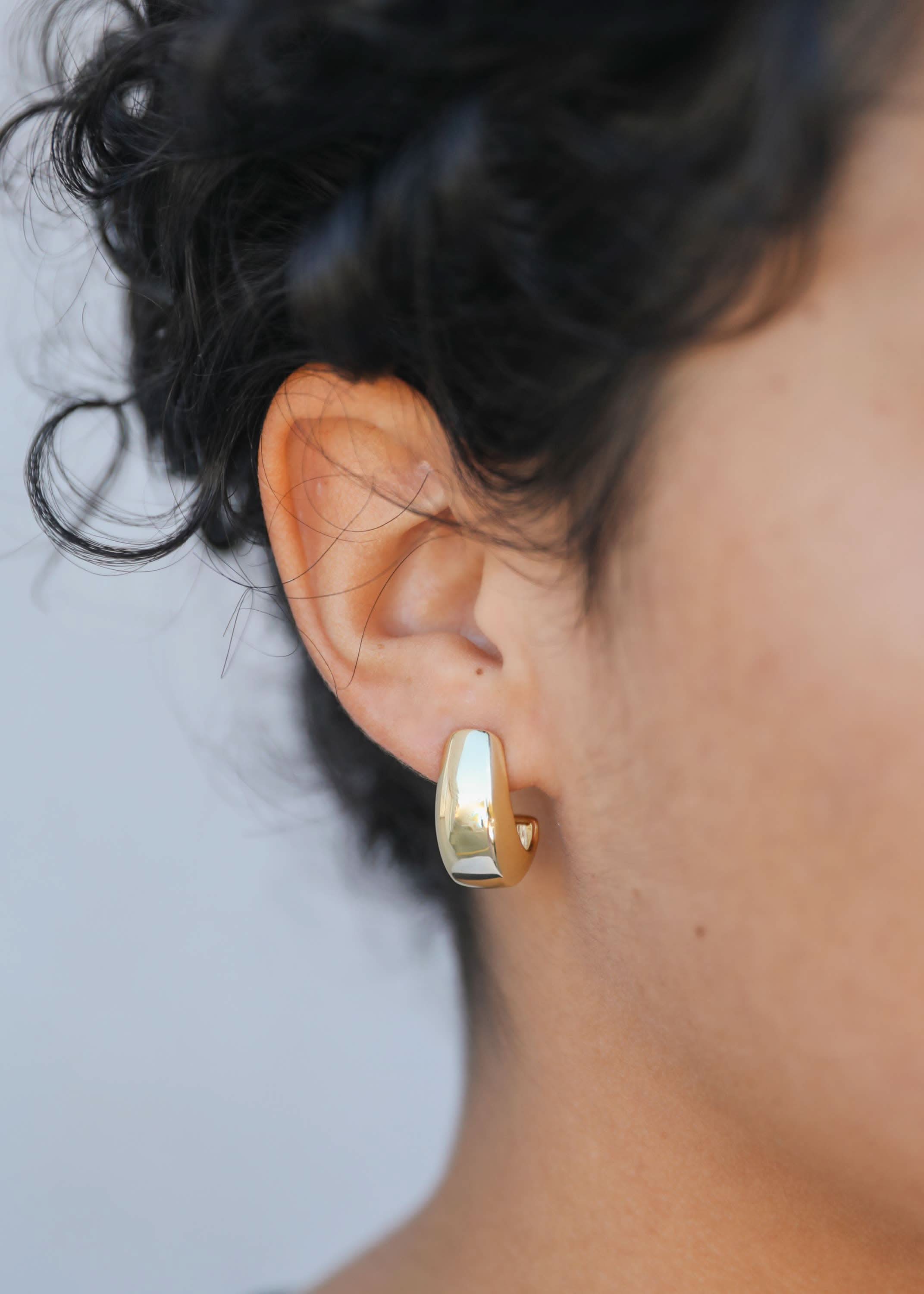 Close-up of a person wearing a gold hoop earring with a blurred background