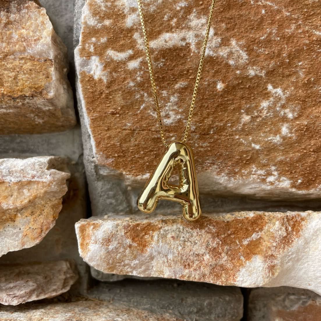 Gold necklace with a 'A' pendant on a stone background