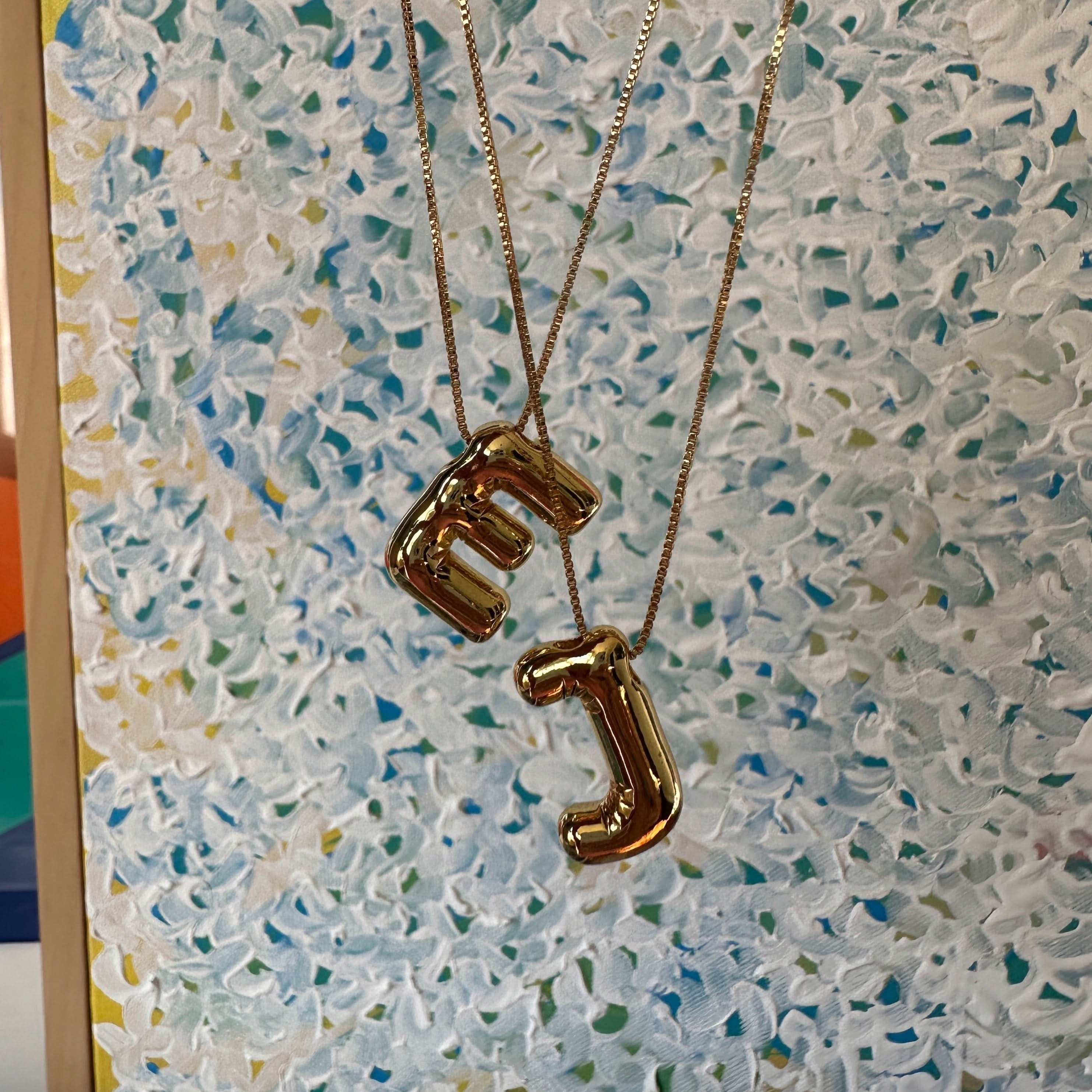 Gold necklaces with letter E & J pendants on a textured surface