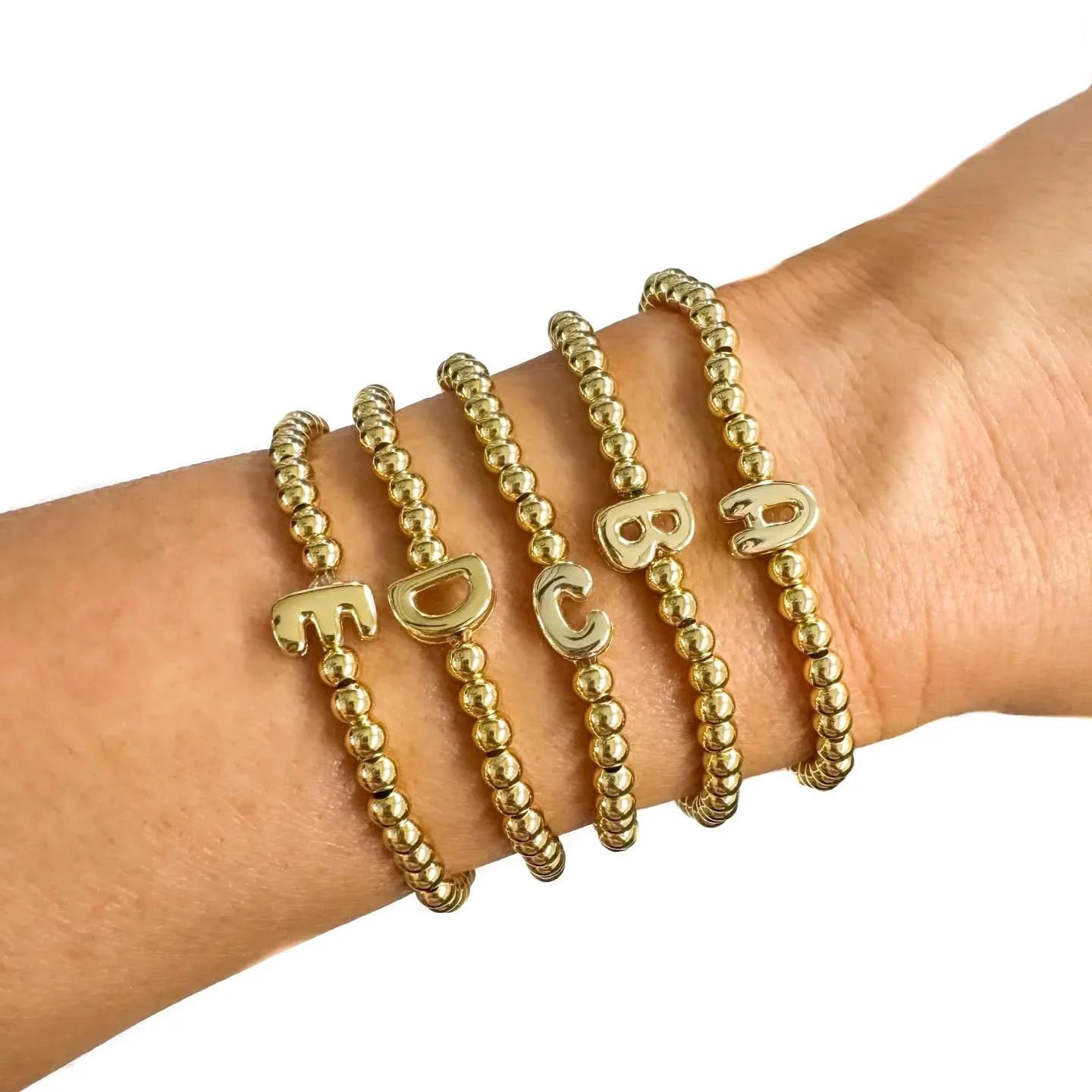 Gold beaded bracelets with letter charms on a wrist against a white background