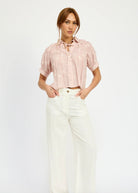 Model standing against a white background wearing white jeans and a pink flowy blouse with tulip embroidery details