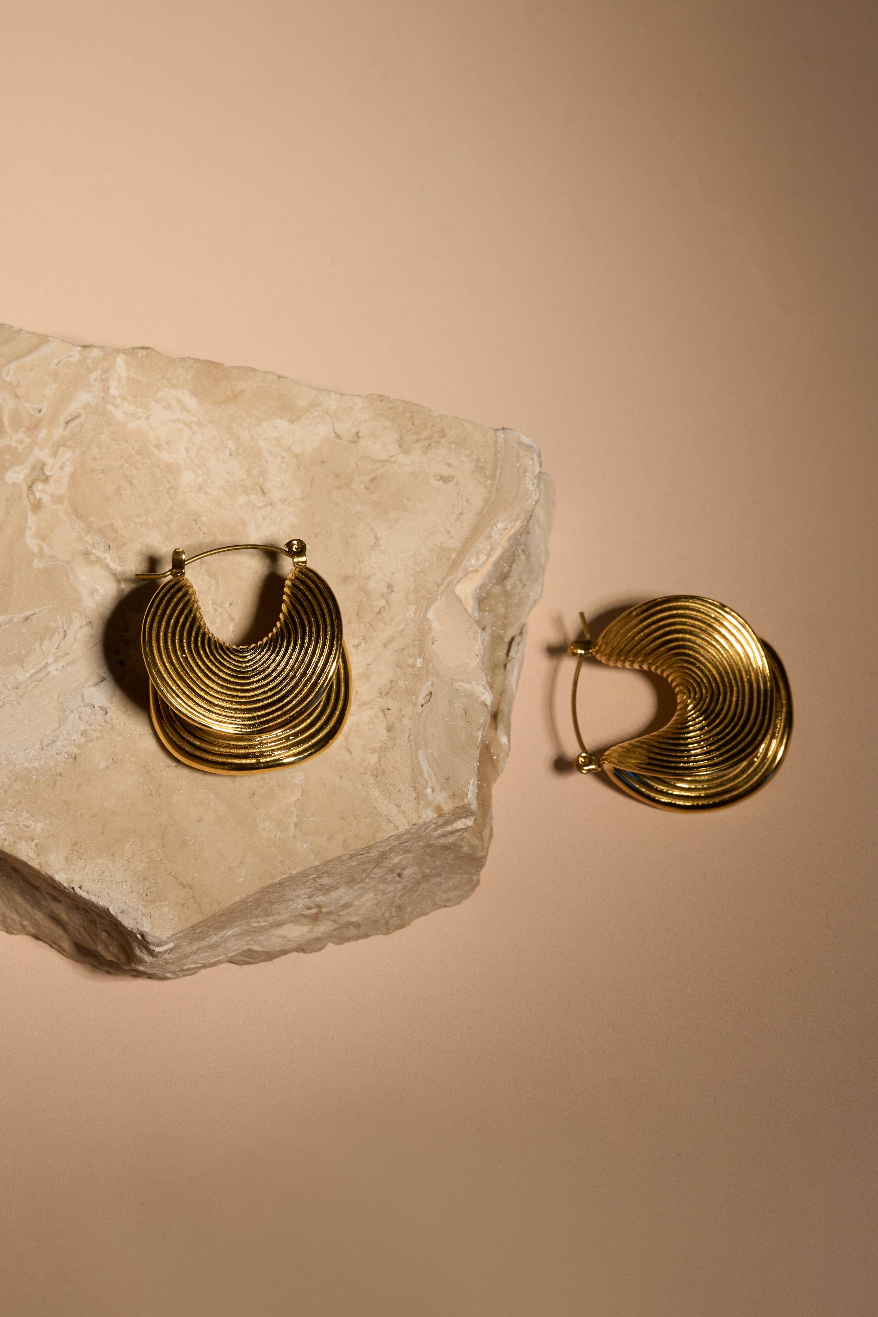 Gold hoop earrings on a stone surface with a beige background