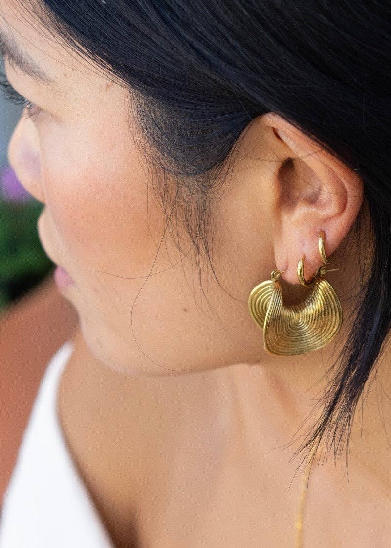 Close-up of a person wearing gold hoop earrings with a blurred background