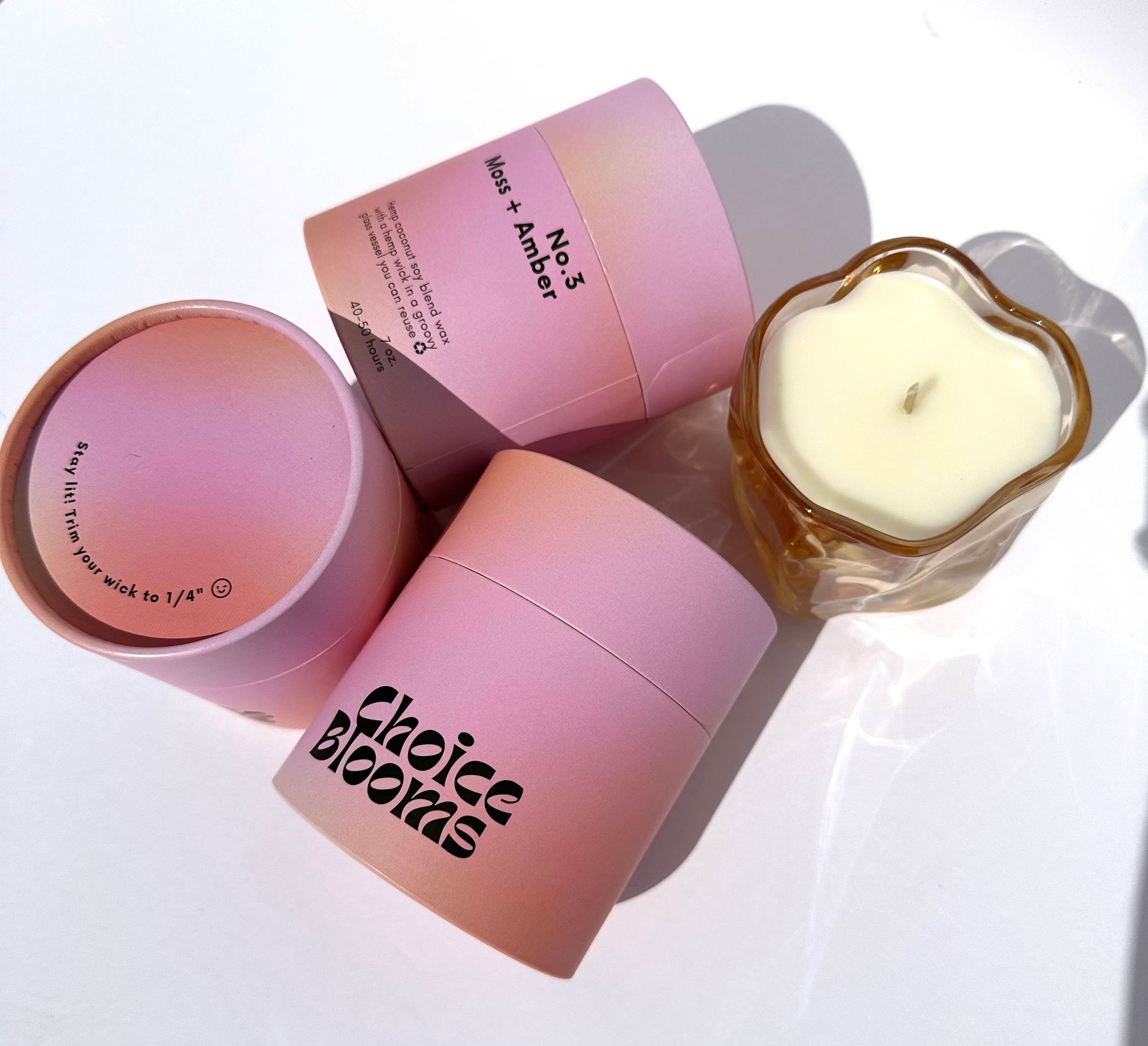 One candle in a pink wavy glass container next to pink 3 candle packaging containers 
