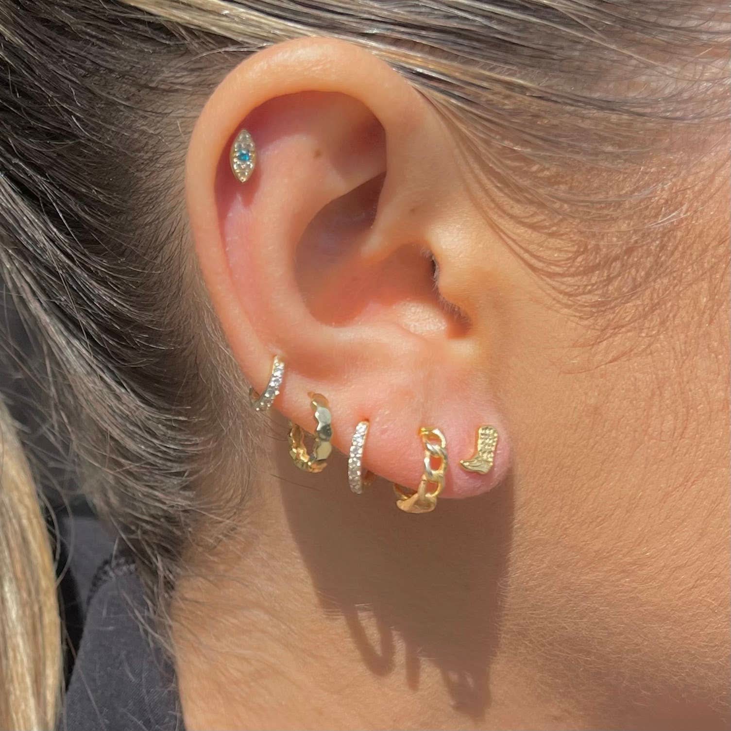 Close-up of an ear with multiple gold and silver hoop earrings.