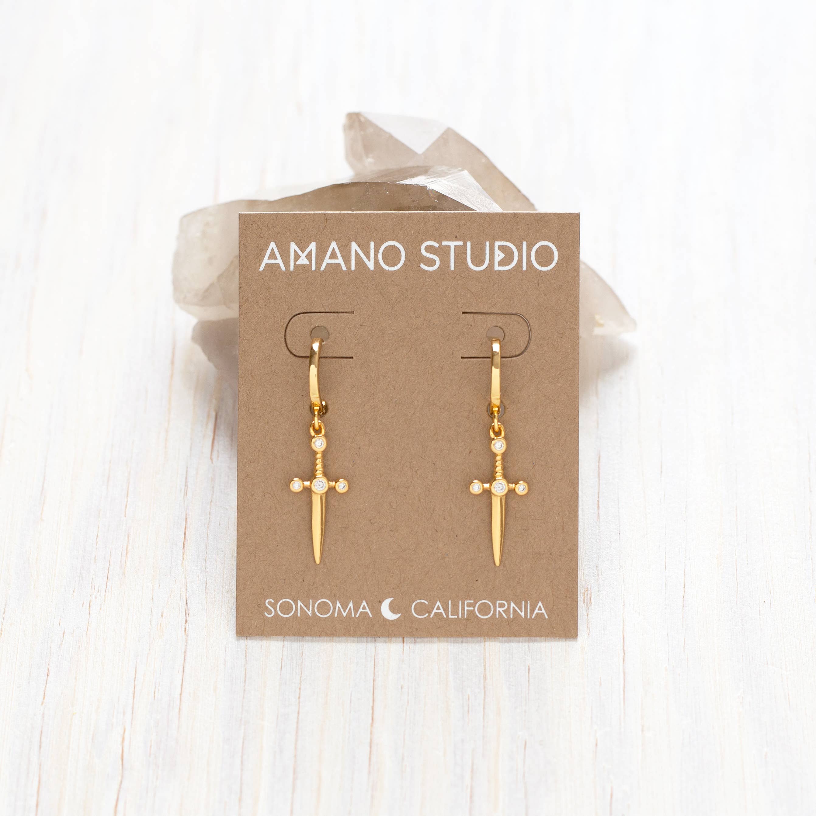 Gold earrings on a 'Amano Studio' branded card with a white background