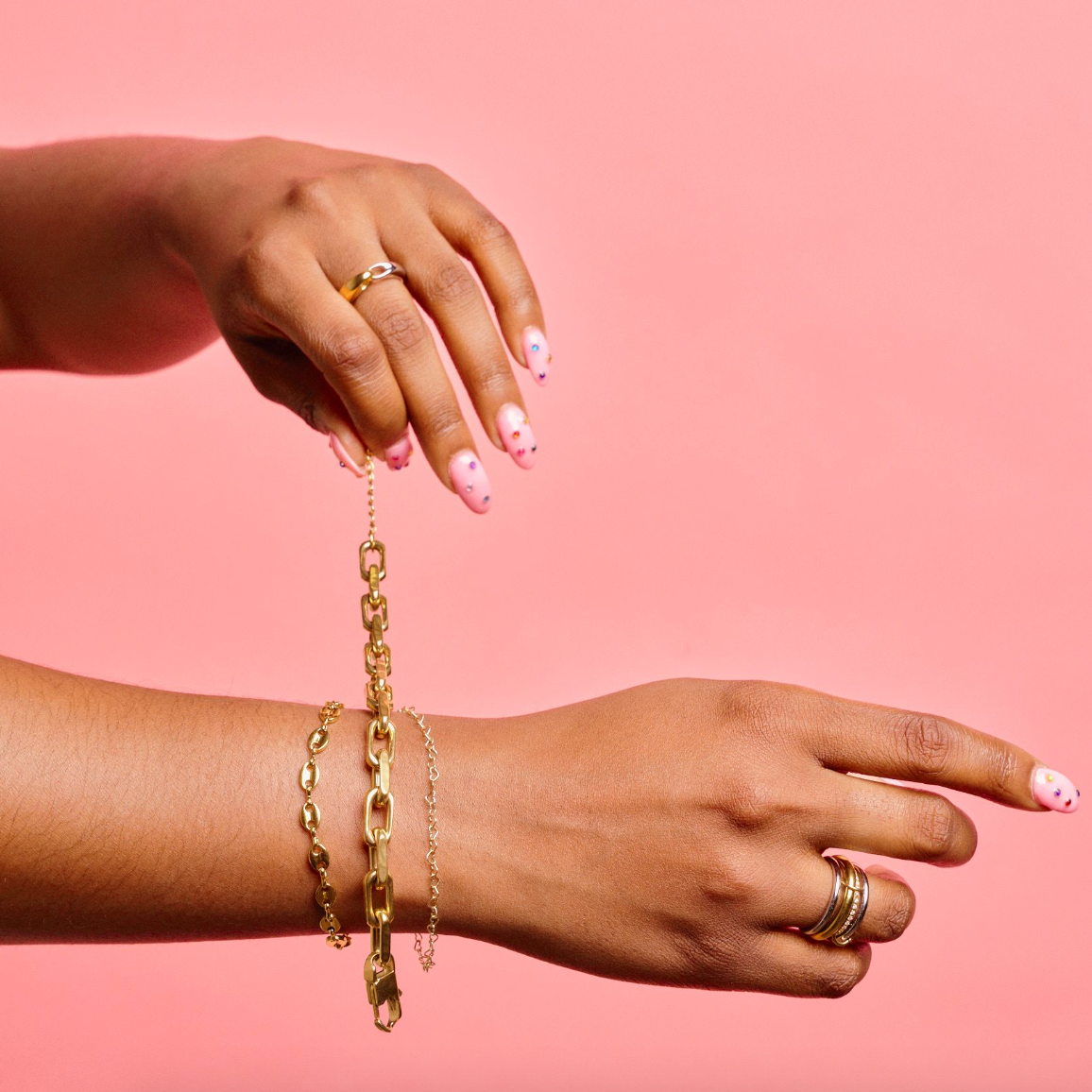 Woman putting on a Gold, waterproof, chunky link bracelet from Nikki smith against a pink surface 