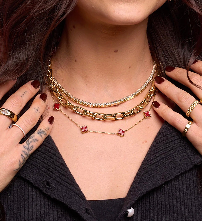 Close-up of a person wearing multiple gold necklaces with red pendants.