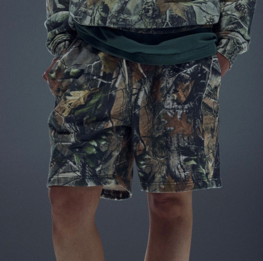Person wearing camouflage shorts and a jacket on a gray background
