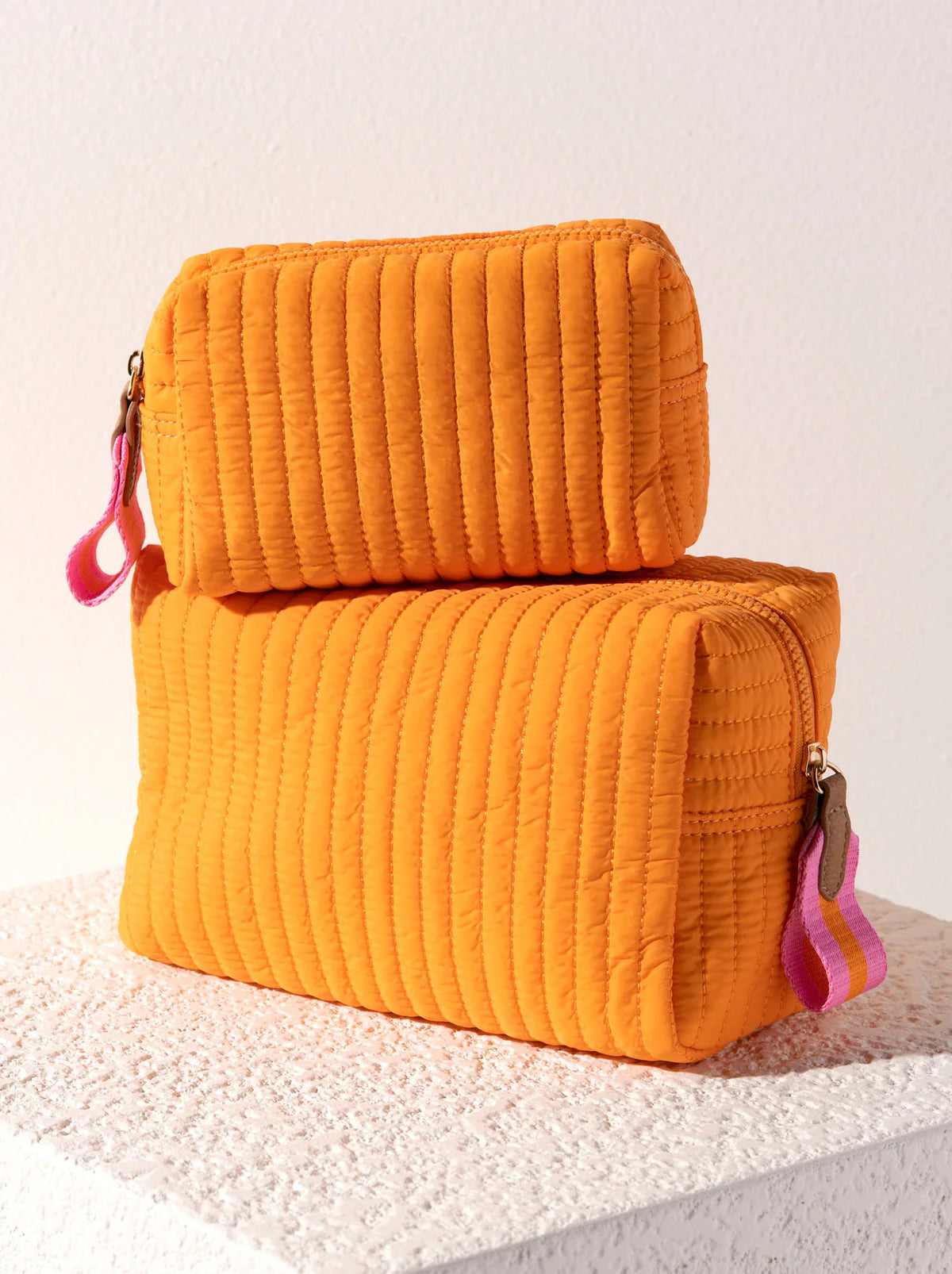 Two orange quilted pouches with pink zippers on a textured surface.