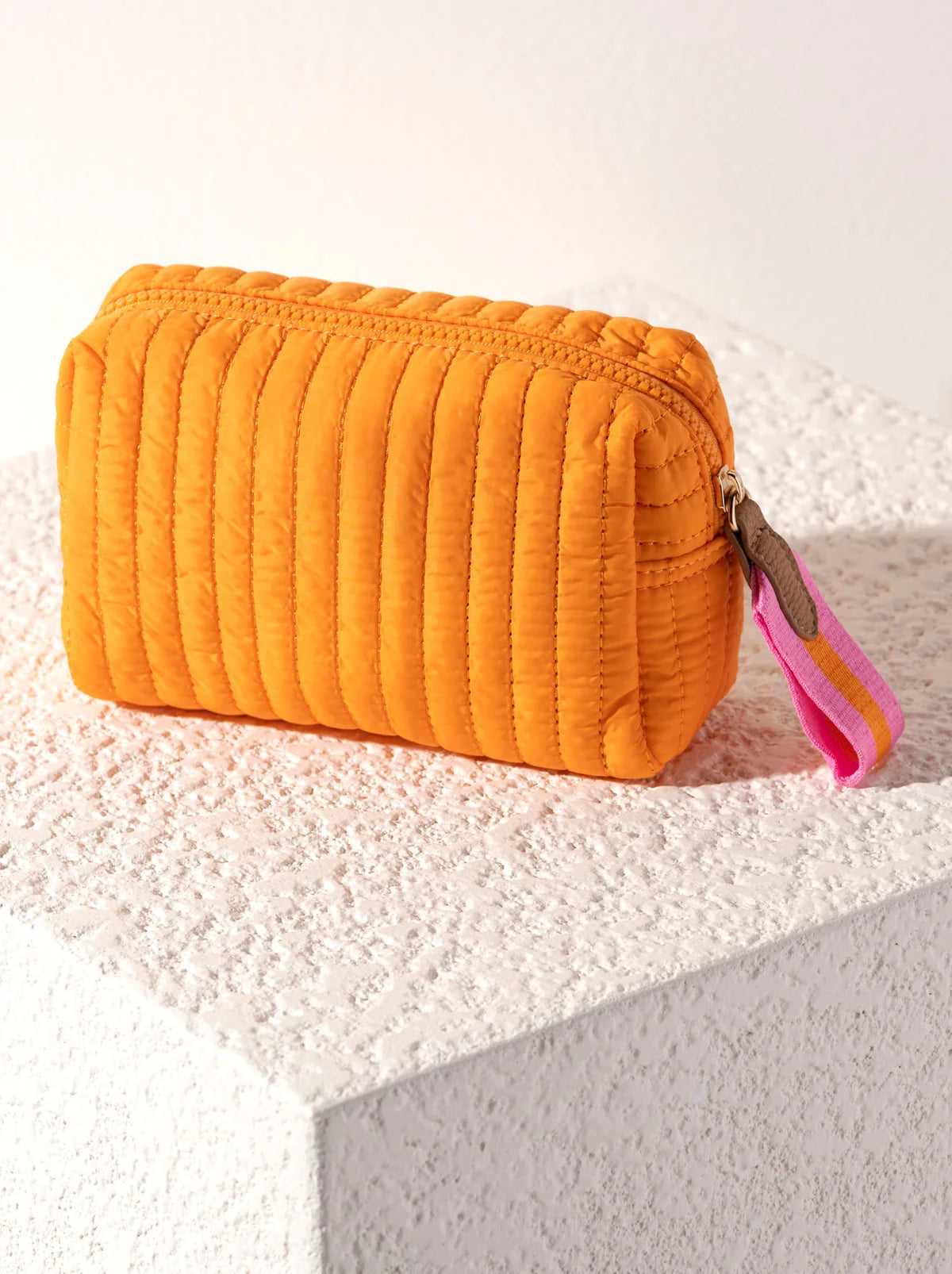 Orange quilted cosmetic bag with a pink strap on a textured surface