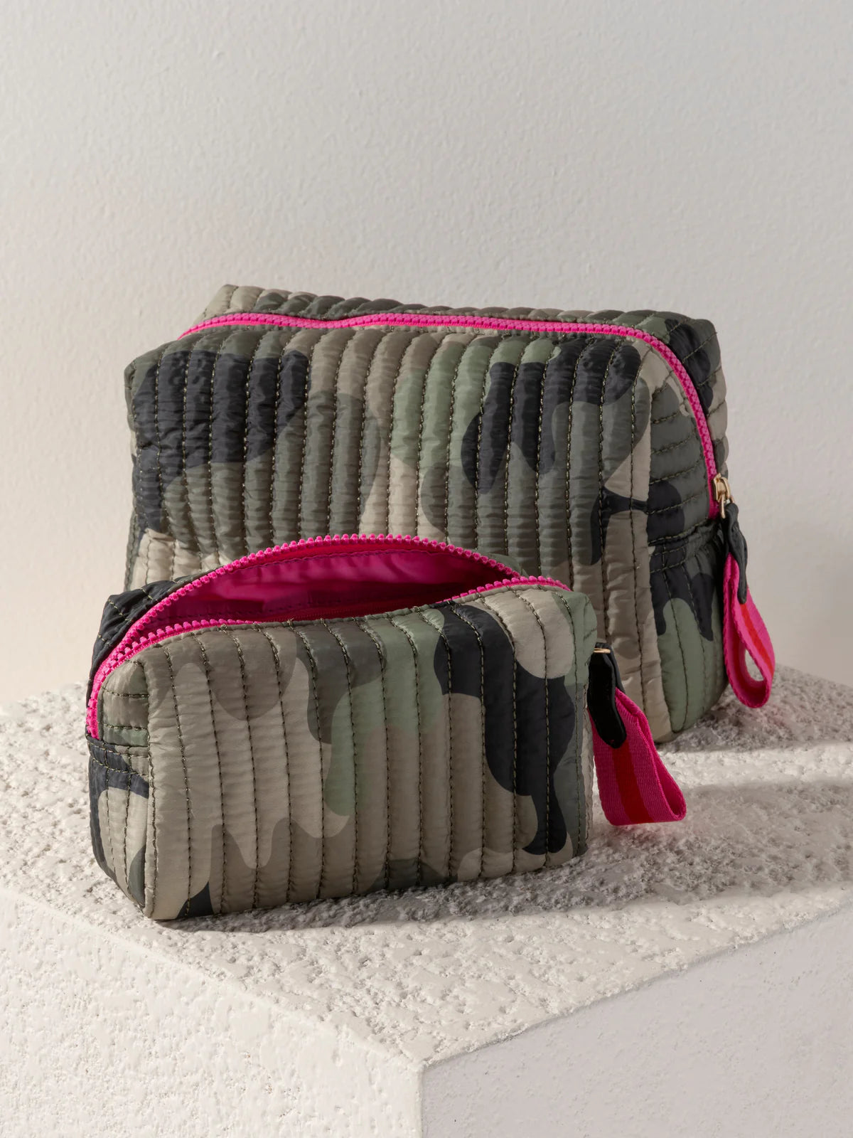 Two camouflage-patterned pouches with pink zippers on a textured surface.