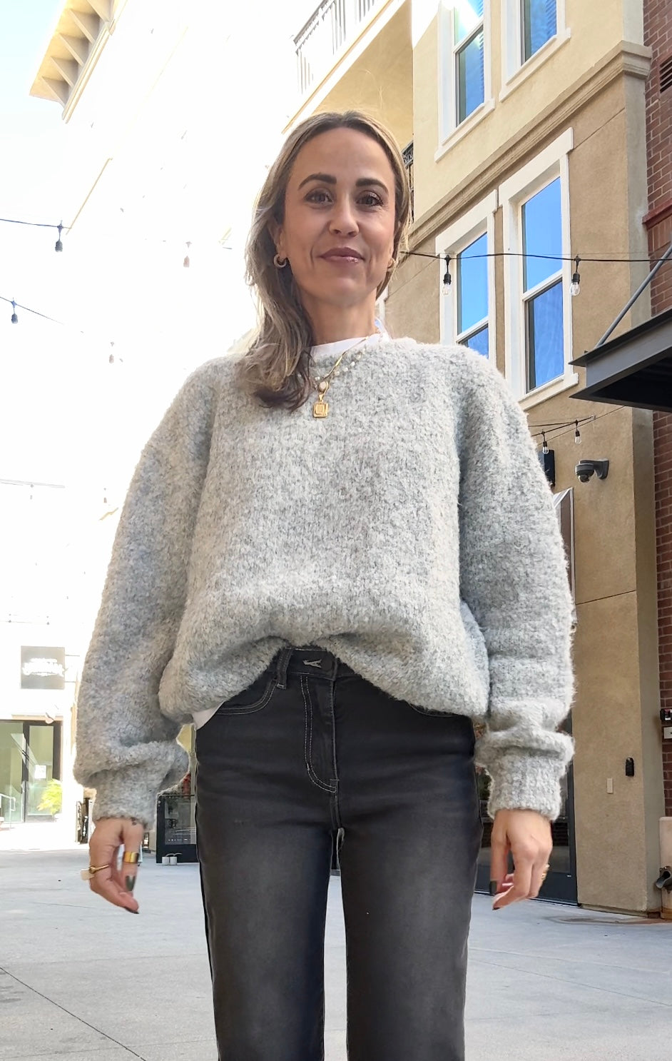Woman wearing a light gray sweater and dark jeans on a city street.