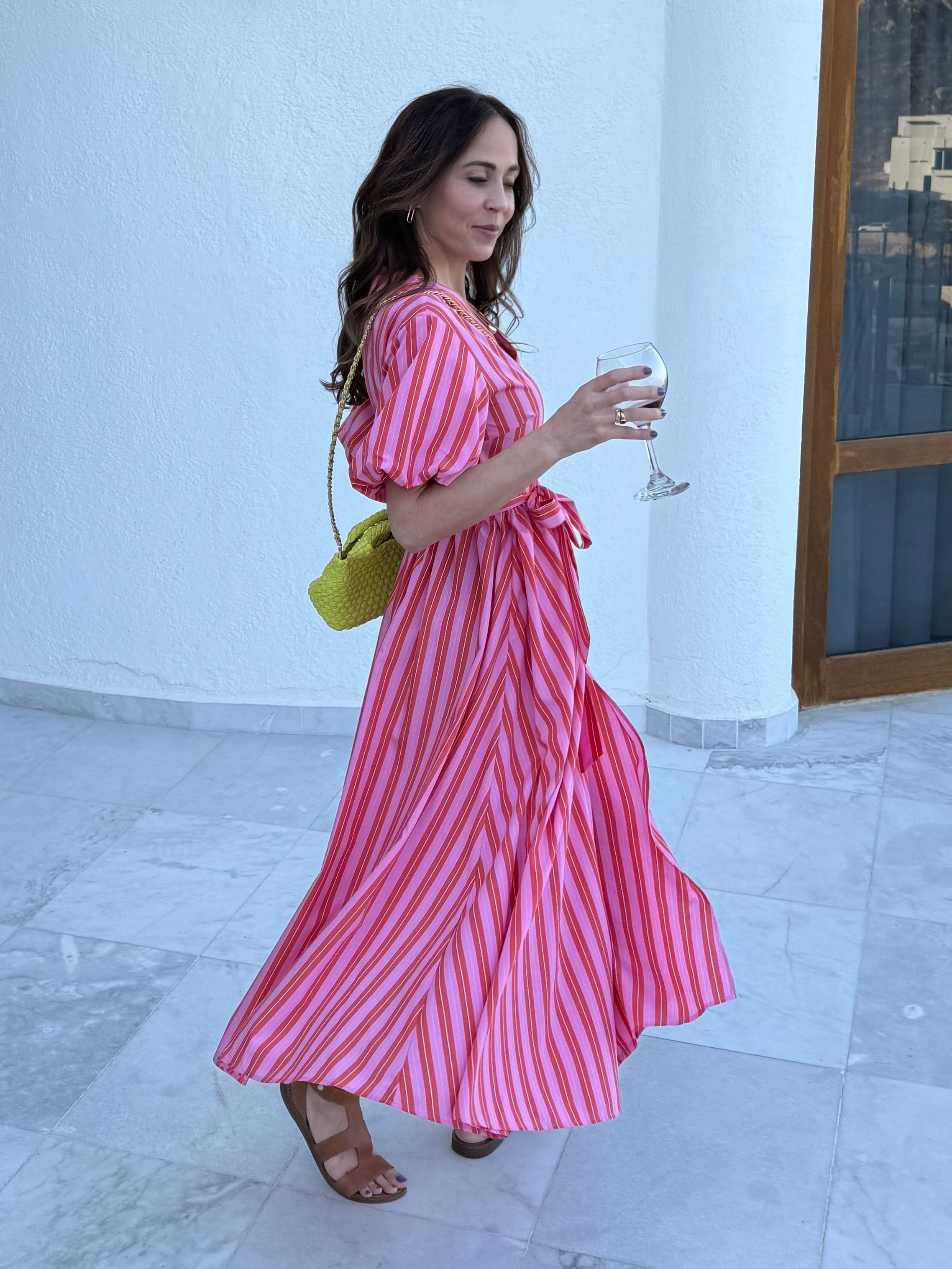 Woman in a pink and white striped dress holding a glass of wine indoors.
