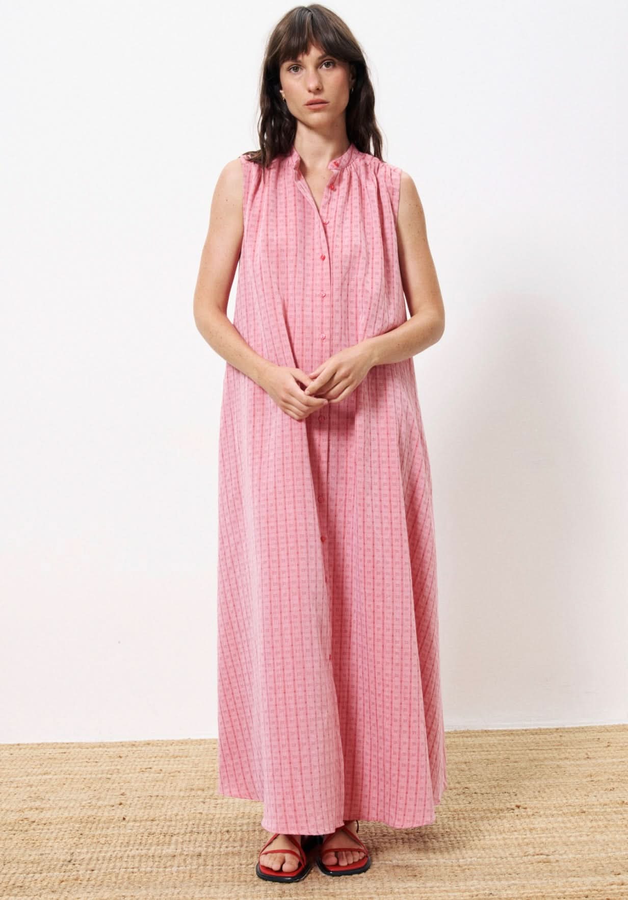 Woman wearing pink dress with buttons all the way down and square geometrical pattern, wearing red  sandals. frnch clothing