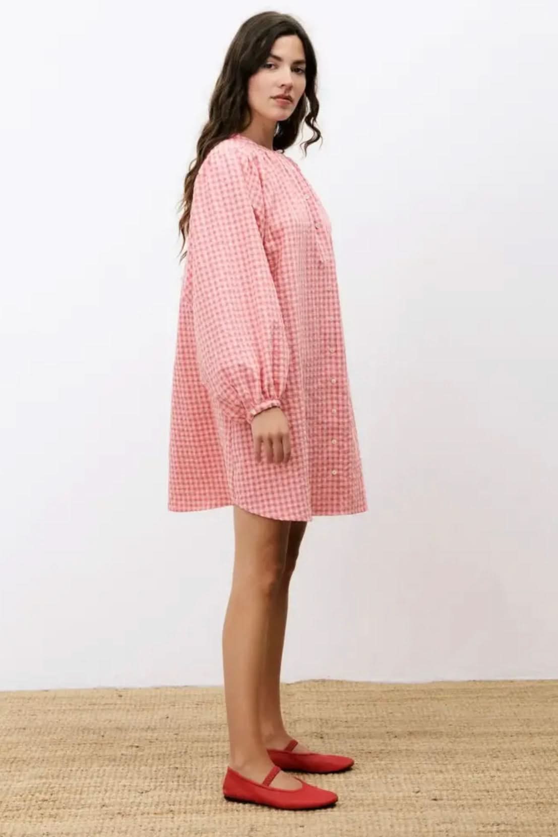 Woman wearing a pink checkered dress with long sleeves on a white background